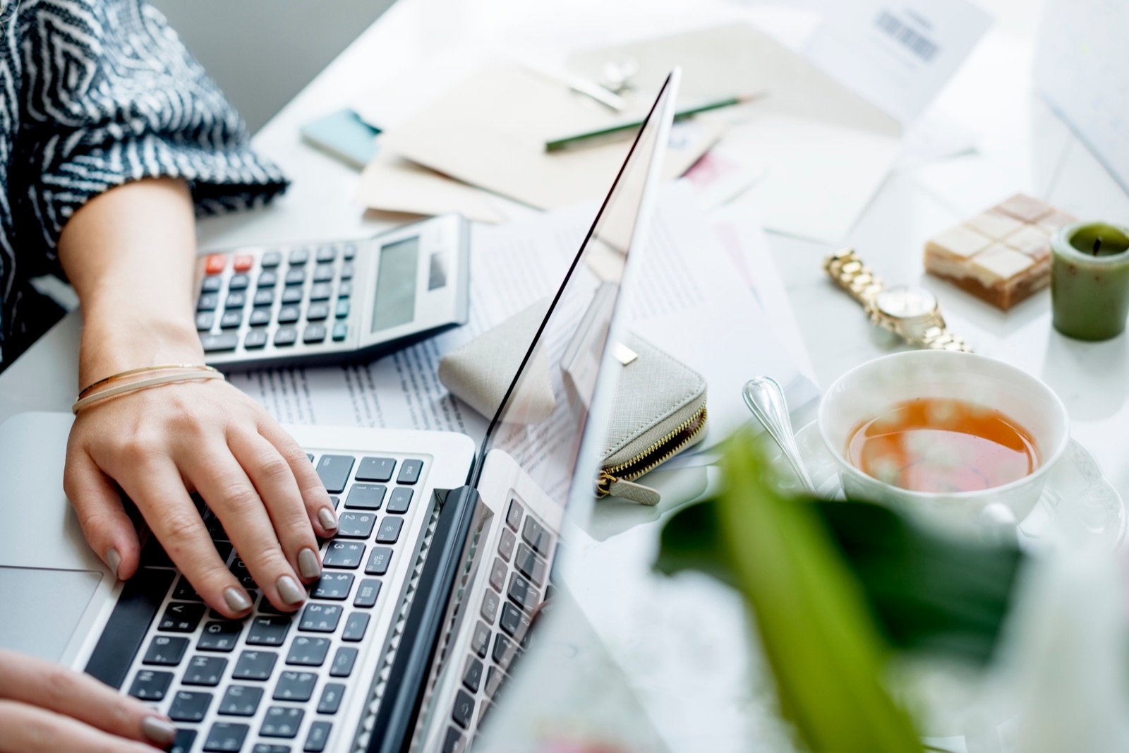 Business owner working on a laptop beside a calculator and cup of tea